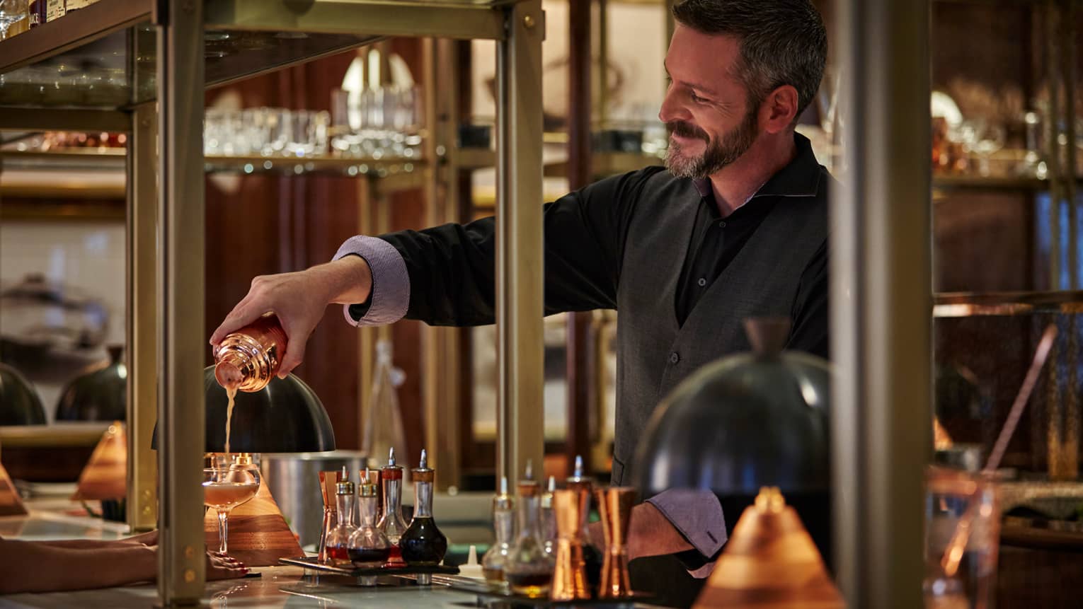dimly-lit,dimly pours cocktail from copper shaker into glass on dimly-lit bar