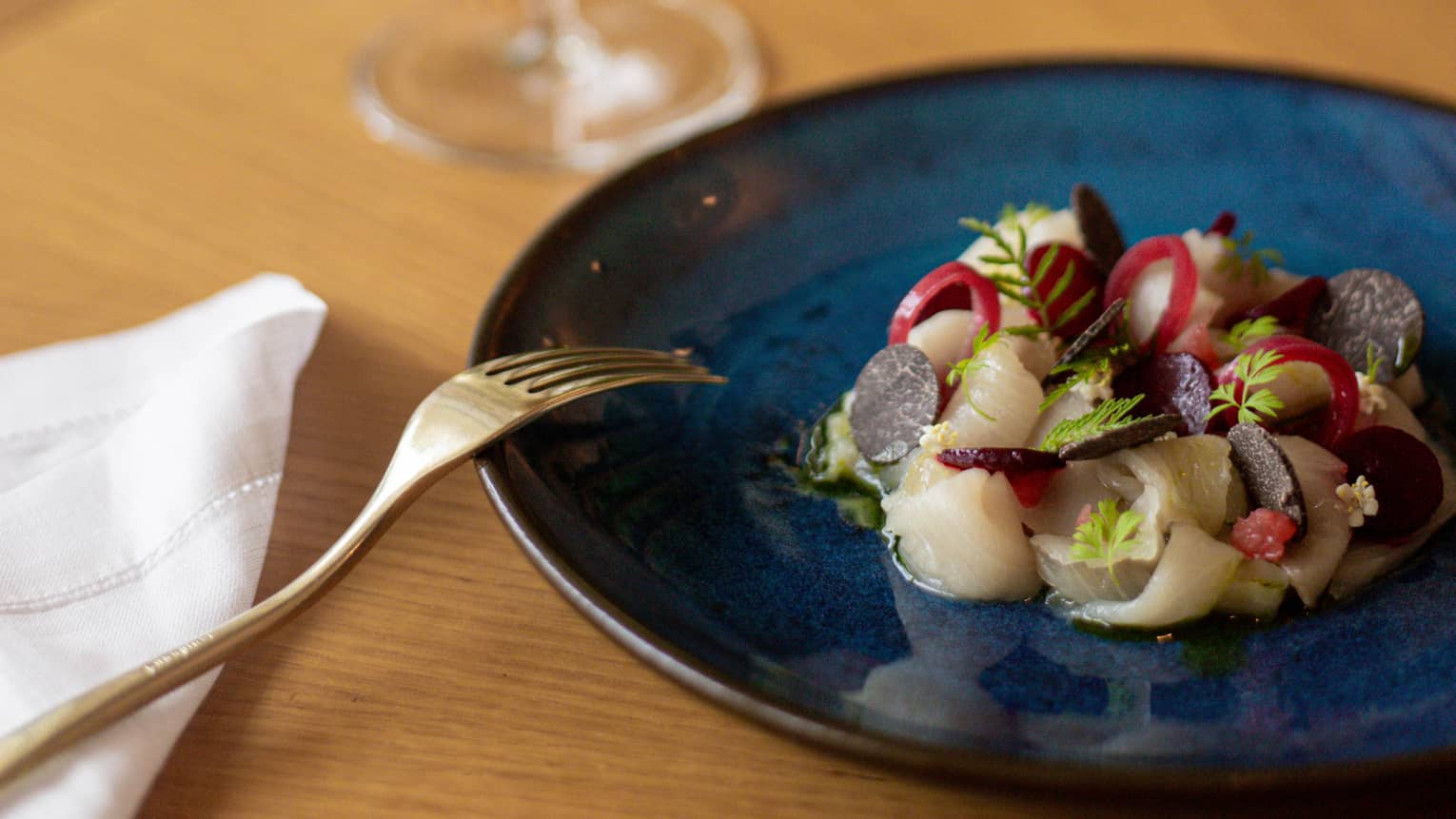 Blue plate of food set next to a glass of white wine and a golden fork