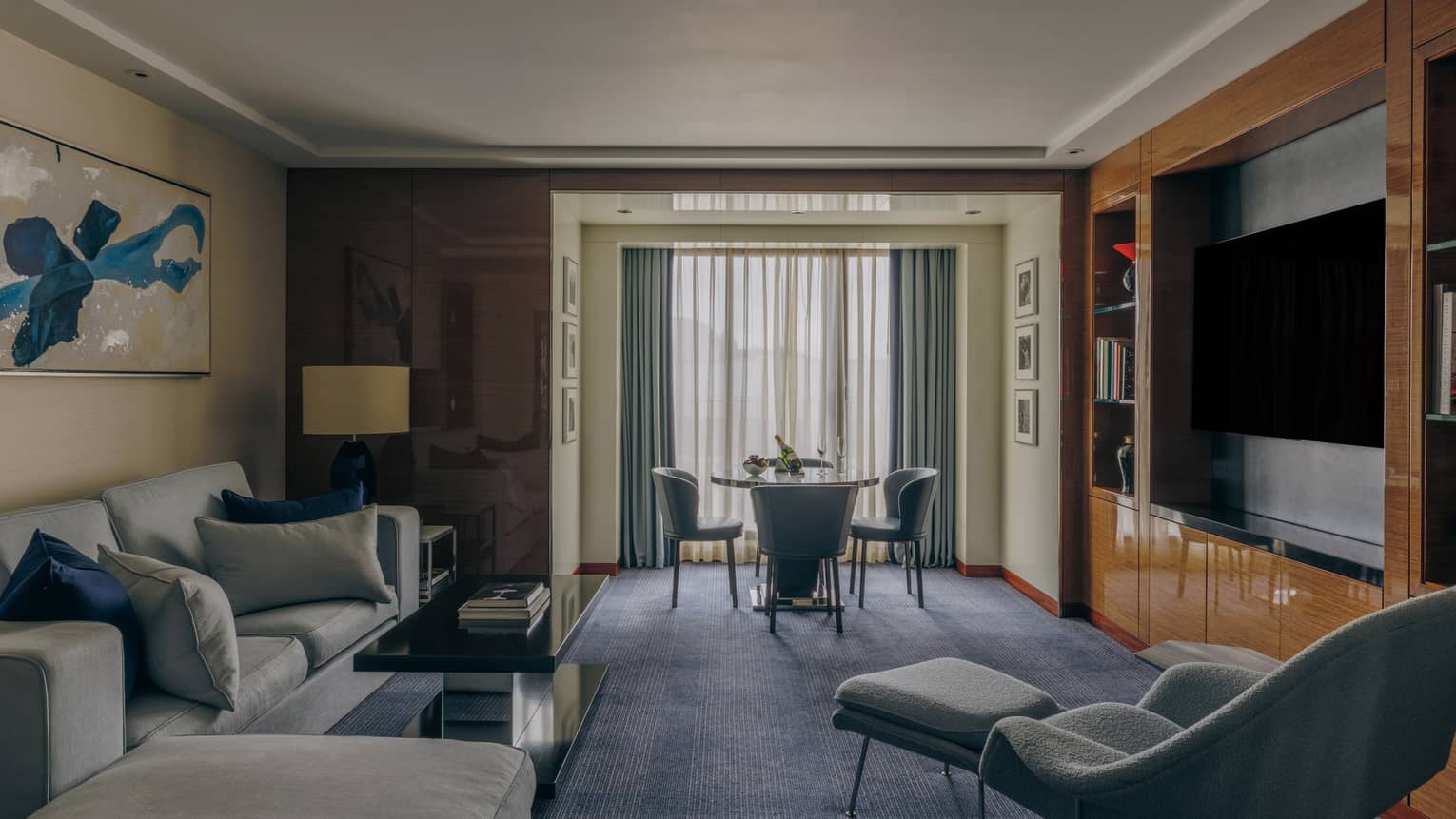 Interior of a luxury hotel suite, featuring a sofa, arm chair, media centre and dining table