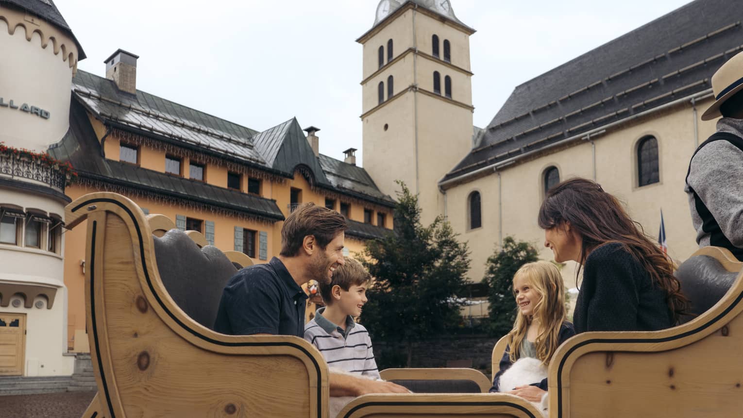 Family of four sitting in a horse-drawn carriage with historic building in background