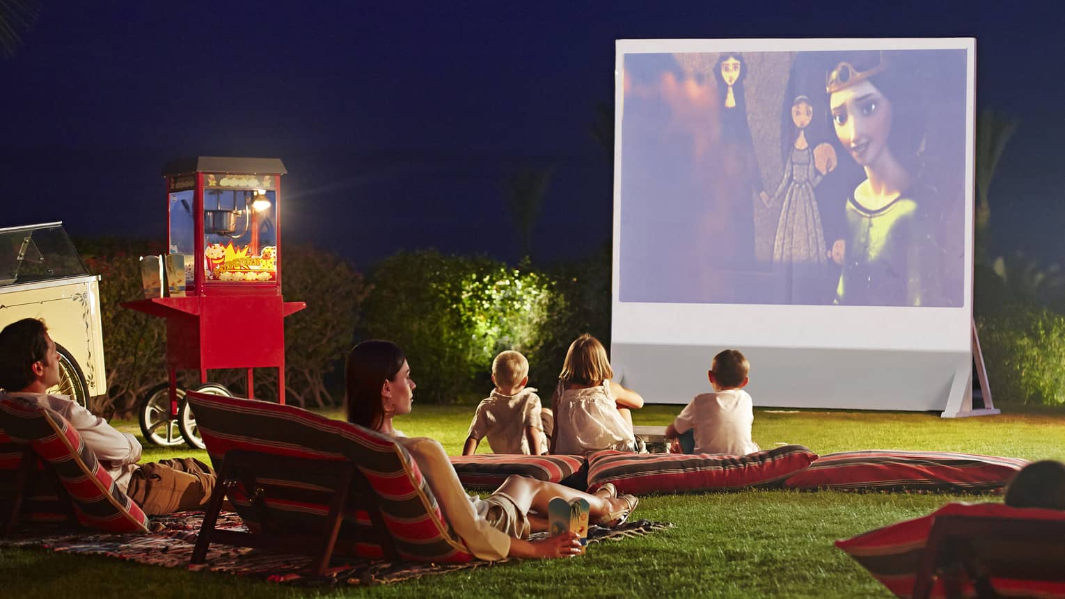 pillows on grass in front of large outdoor movie screen at night