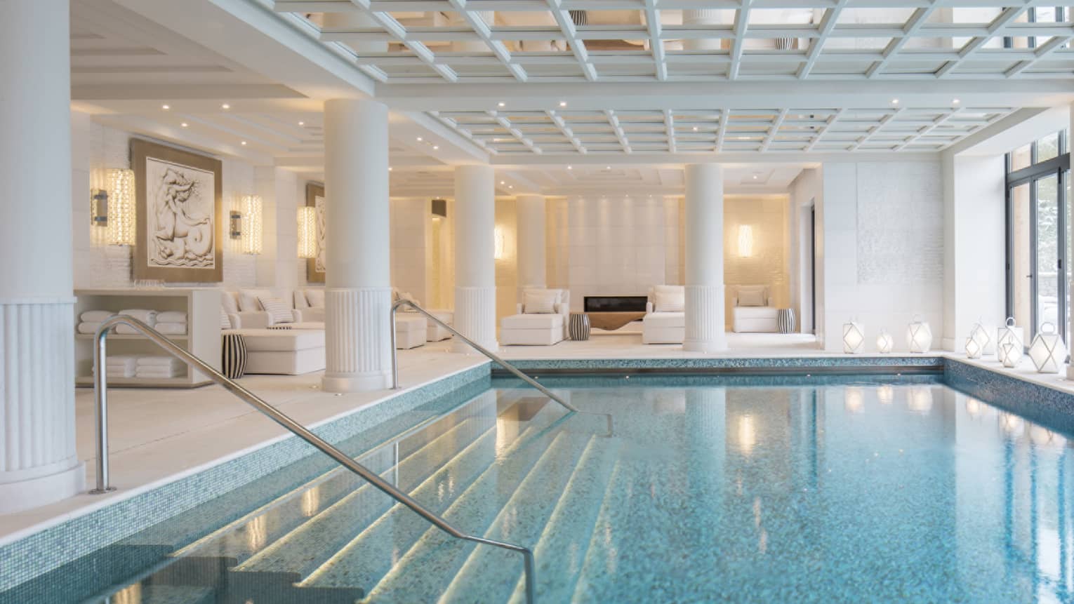 An indoor pool with a glass ceiling above it in a well lit room.