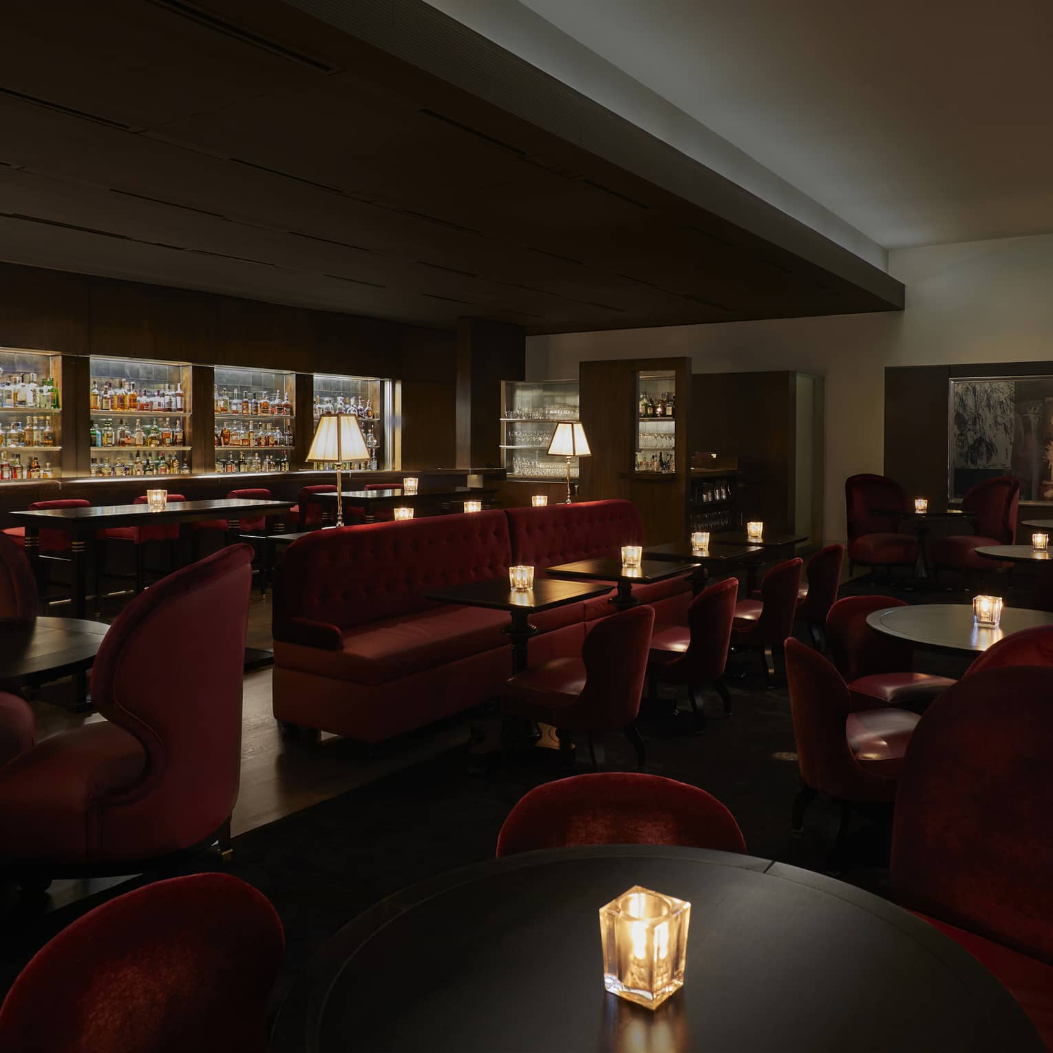 A dimly lit lounge with red chairs and a large selection of drinks behind a bar.