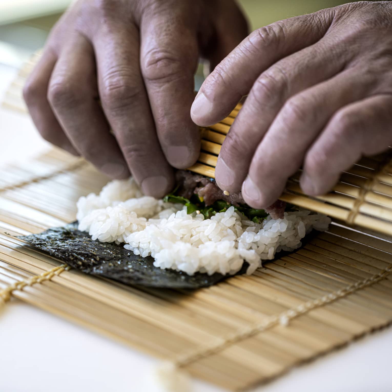 A four seasons chef rolls sushi with a bamboo mat