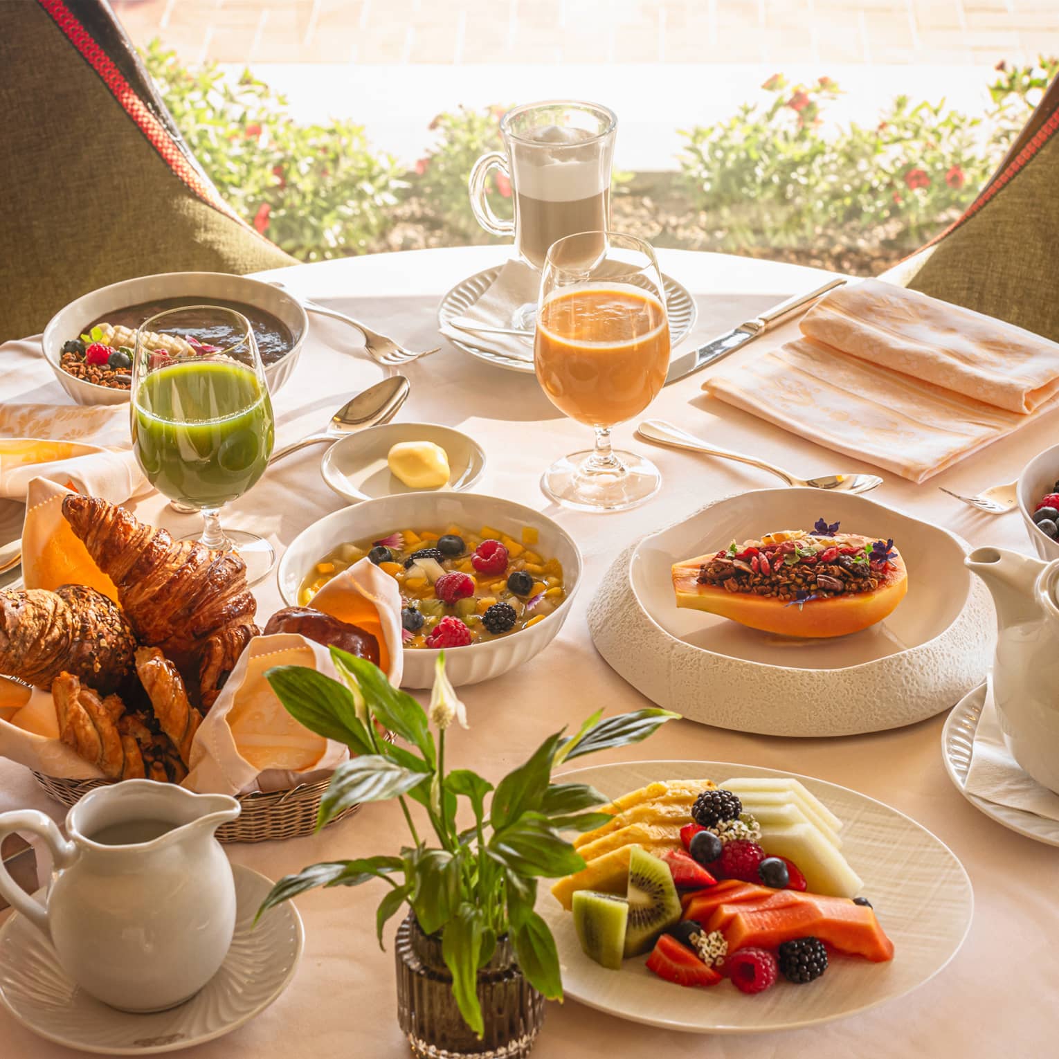 A round table in front of a window, set with an array of brunch dishes and beverages