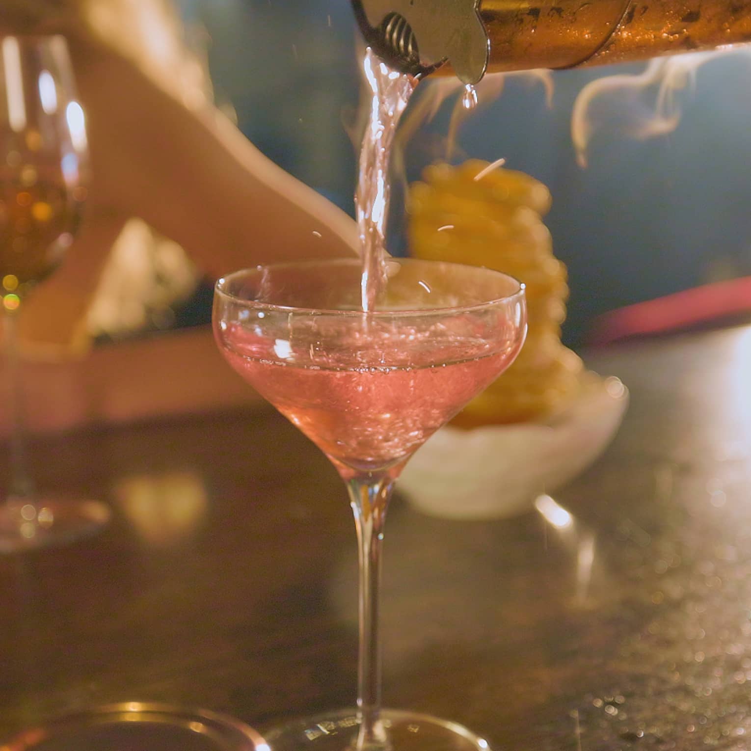 Pink beverage being poured into a cocktail glass