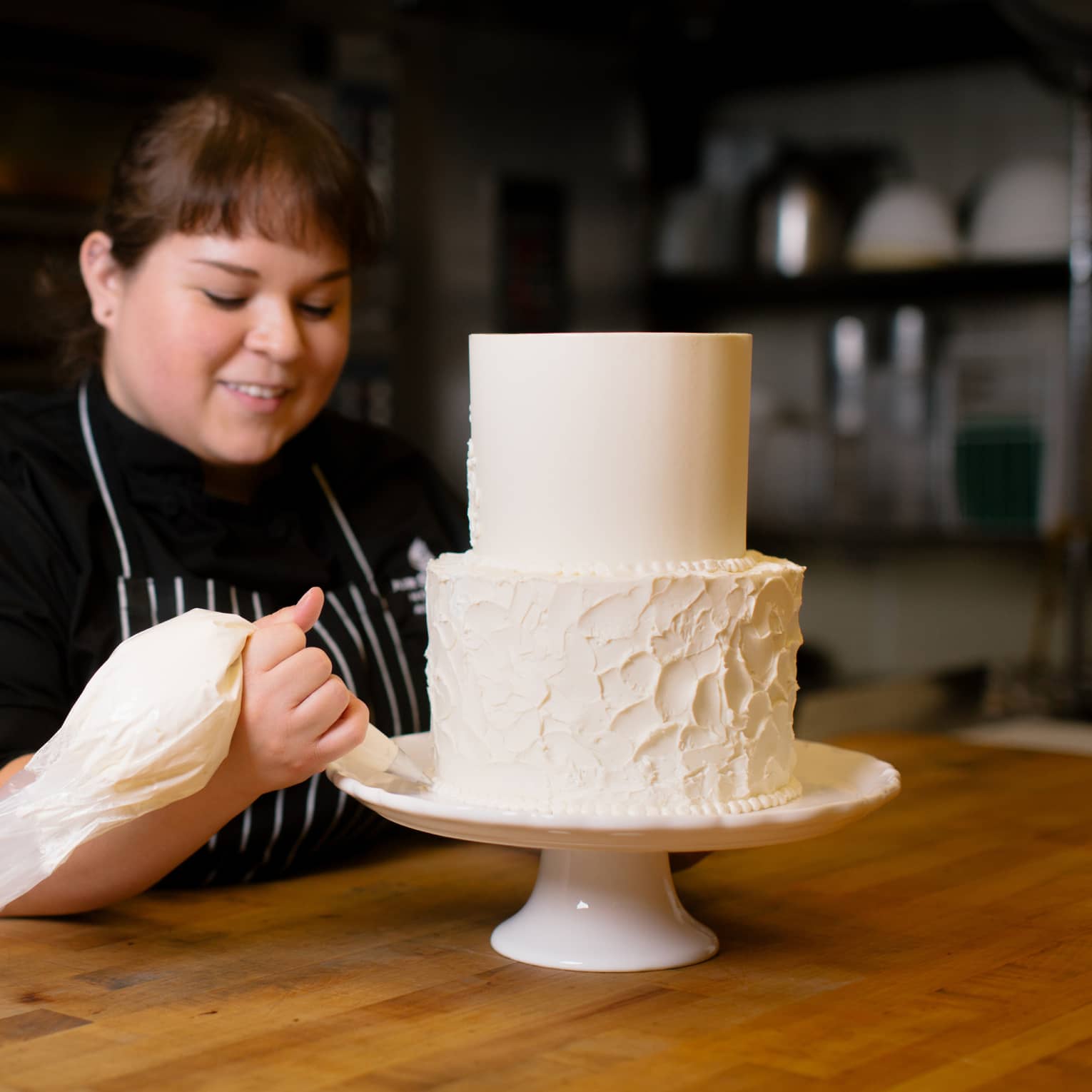 Pastry chef decorates two tiered wedding cake on stand