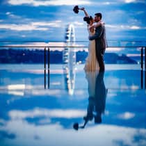 Bride holds up bouquet as she kisses groom at edge of infinity pool, Seattle Great Wheel in background