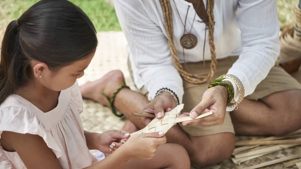 An adult shows a young girl how to weave a basket