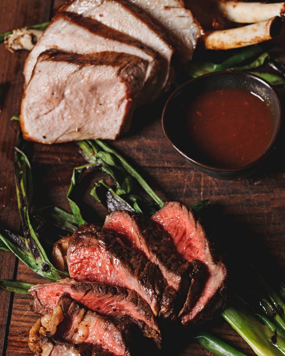 A aerial view of the La Hiki Steak over green onions with a red sauce on the side