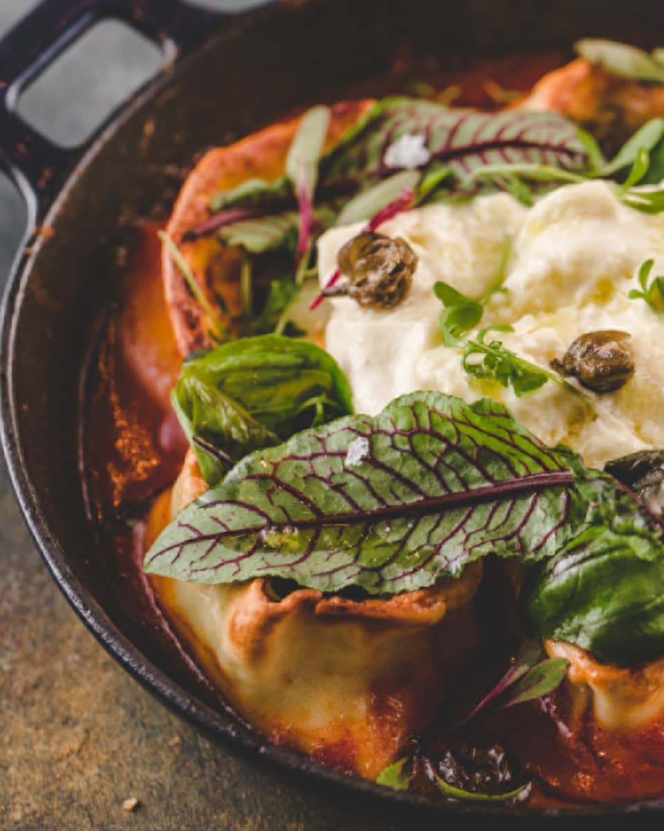 A pasta dish with a tomato sauce, and green leaves on top.