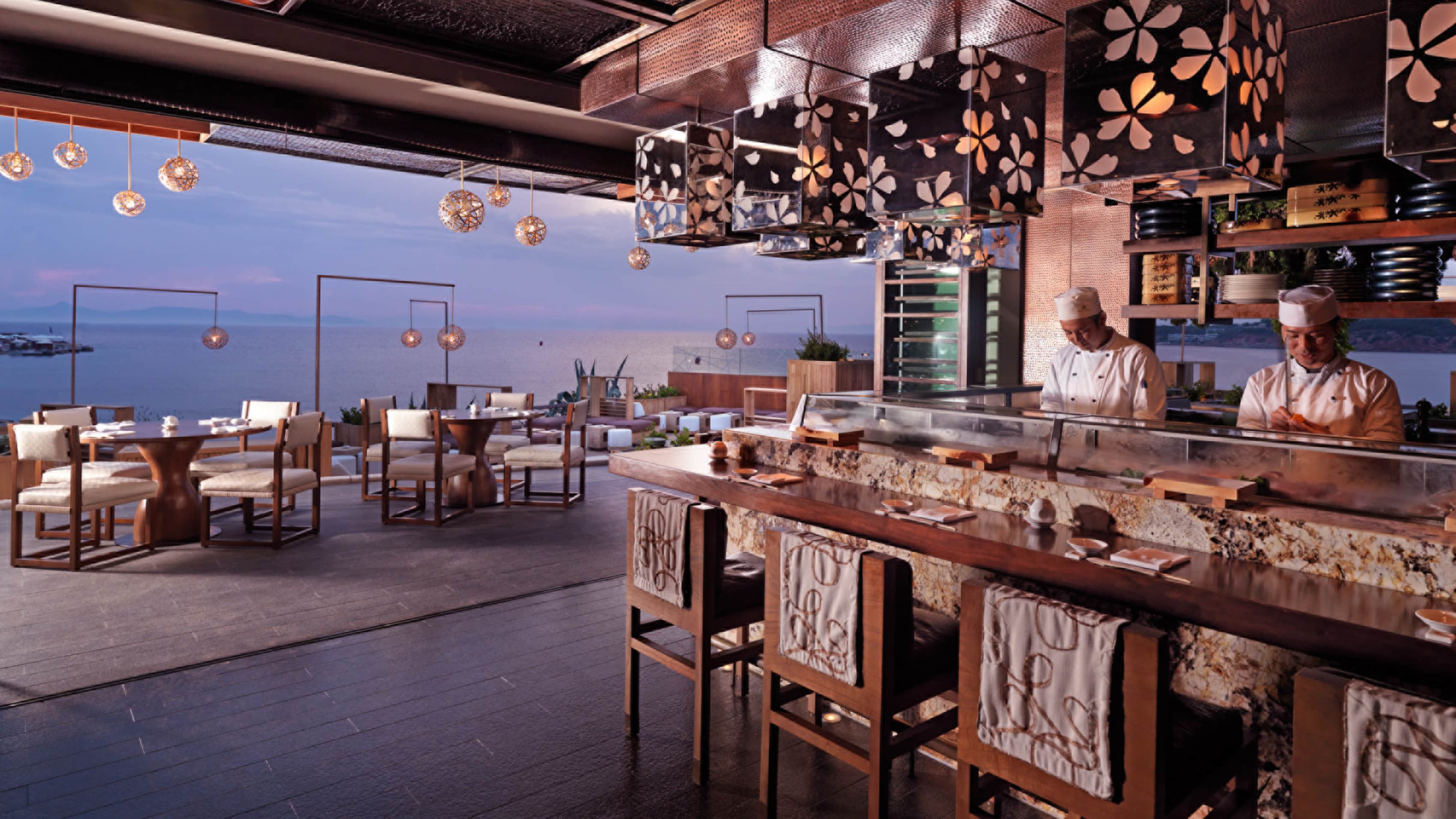 The sushi counter at Matsuhisa Athens, chefs working behind it and the Saronic Gulf through the open wall.