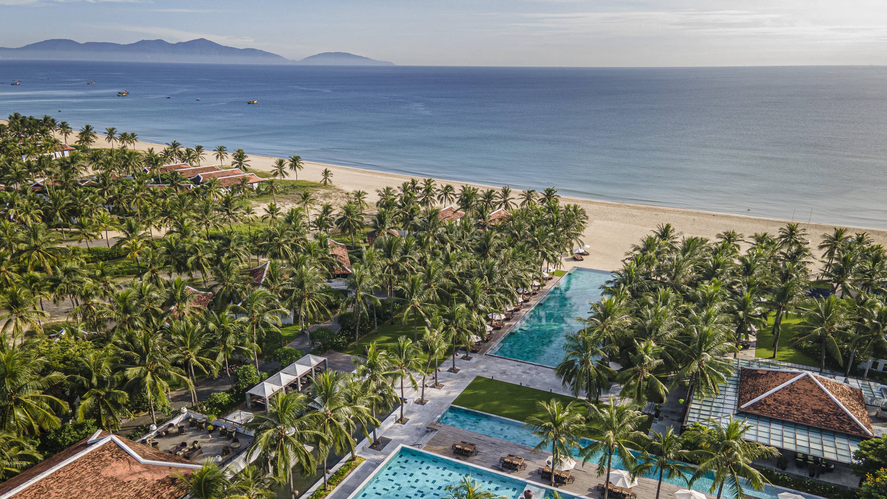 Aerial view of a property with outdoor pools, many trees and the ocean. 