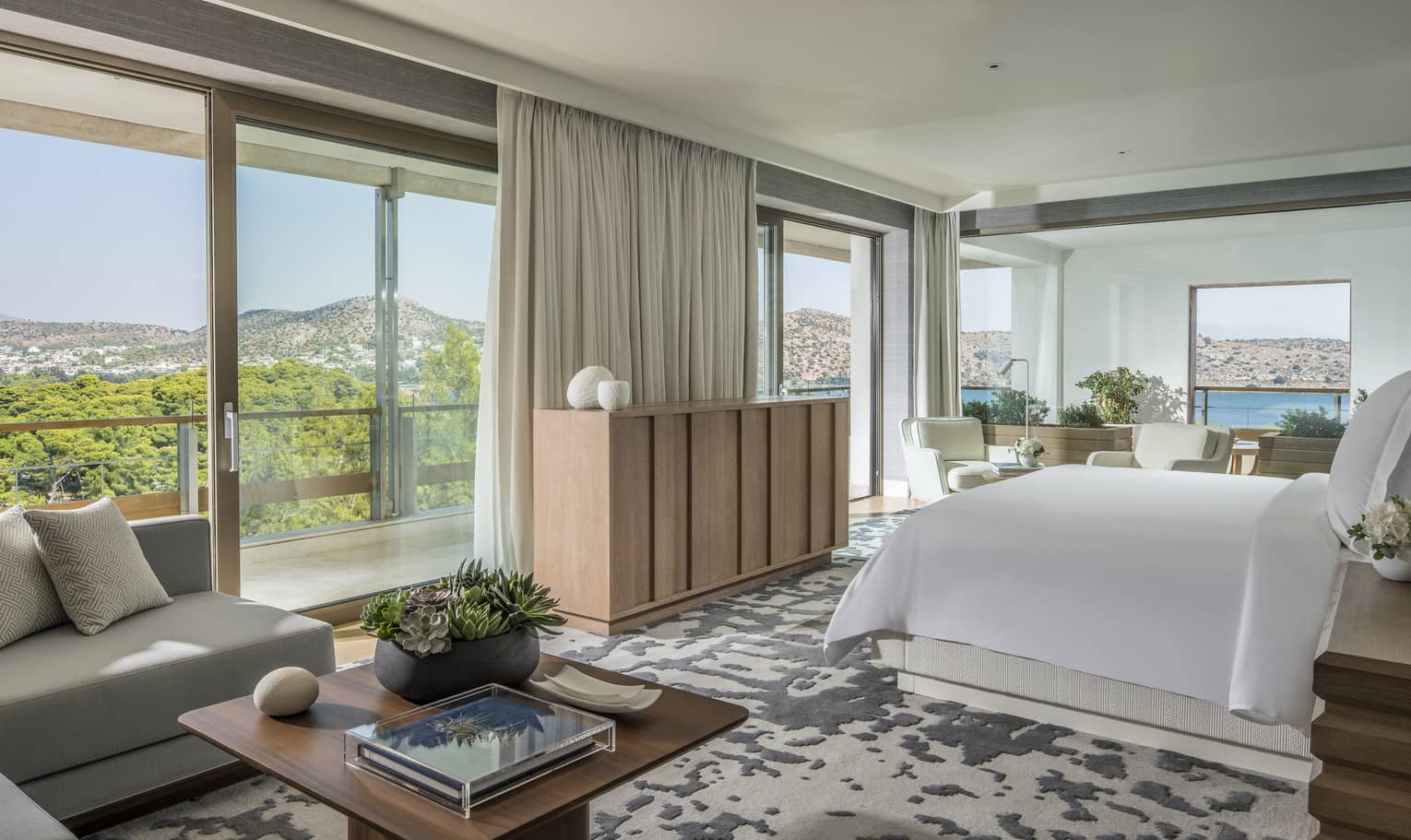 Arion Riviera Suite with white King bed, blonde wood sideboard, grey sectional sofa with square coffee table, panoramic ocean views