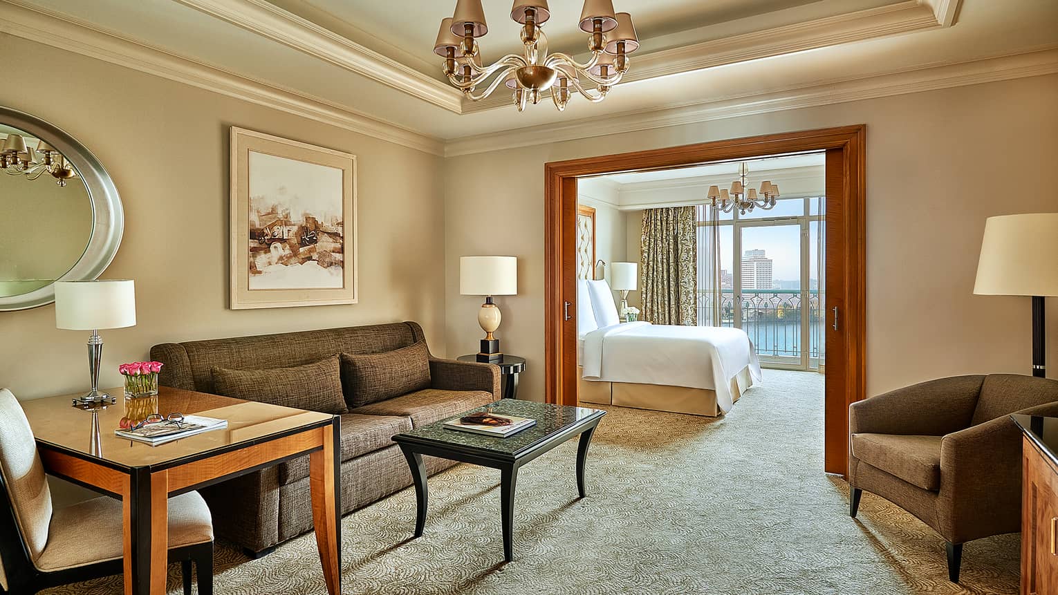 Corniche Suite living room with brown sofa, chairs and desk, door leading to adjoining bedroom