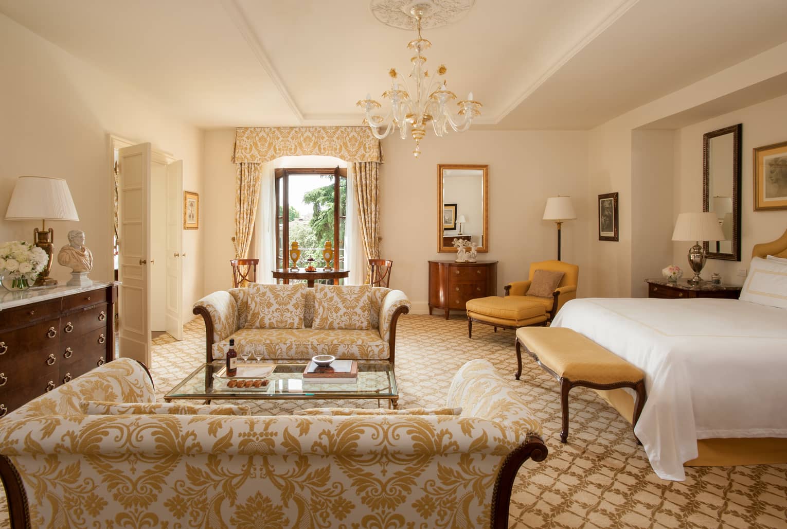 Deluxe Executive Suite gold patterned loveseats under small crystal chandelier, near bed