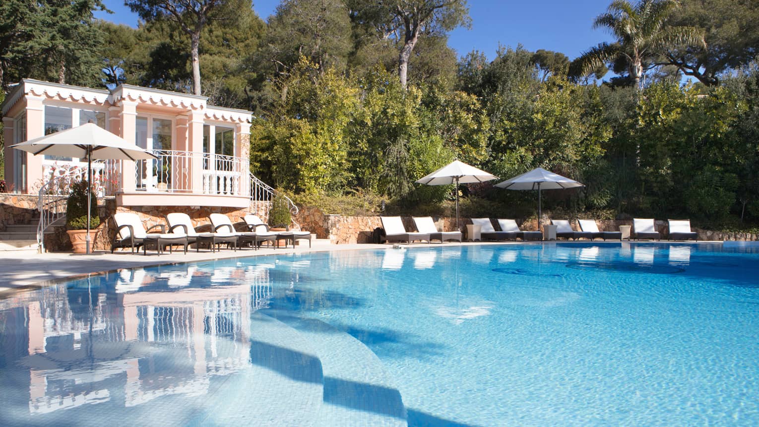 View over blue outdoor swimming pool to deck chairs, villa