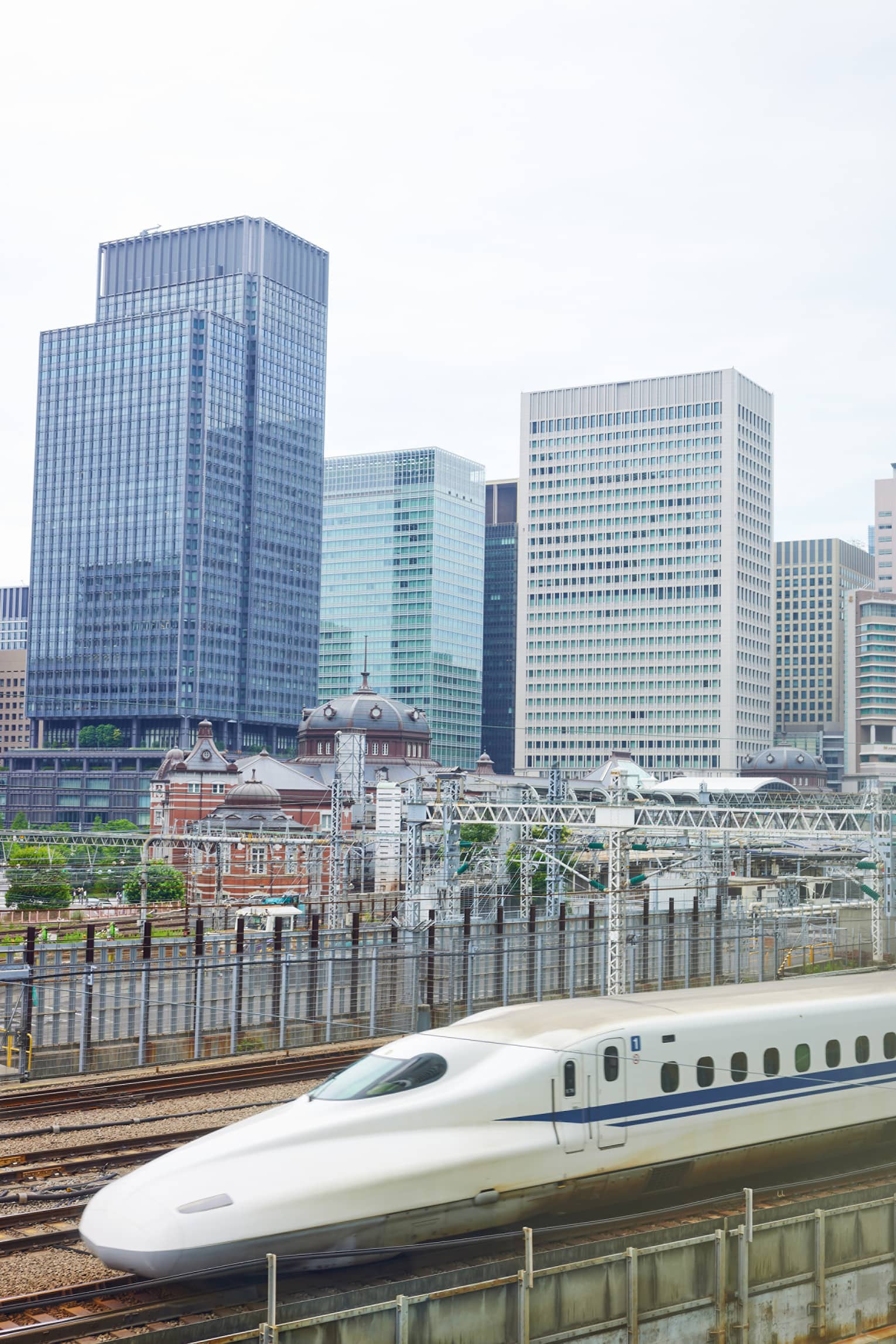 The Shinkansen bullet train speeds past Tokyo's railway station dwarfed by the skyline of rectangular, glass high-rises.