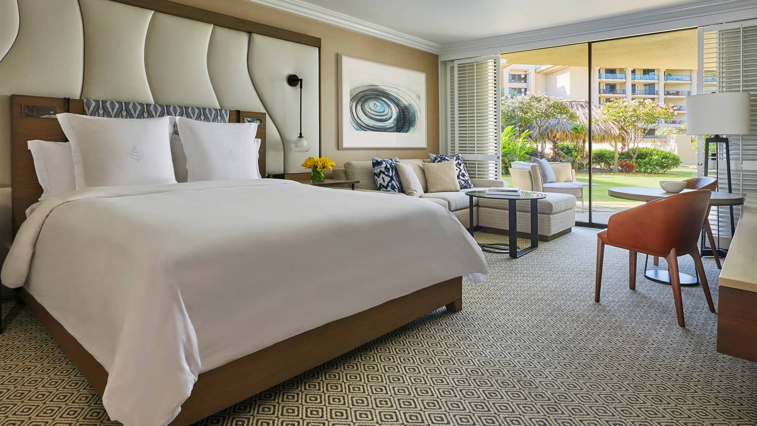 Garden-View room bed with tall padded wall panel, L-shaped white sofa beside glass patio door