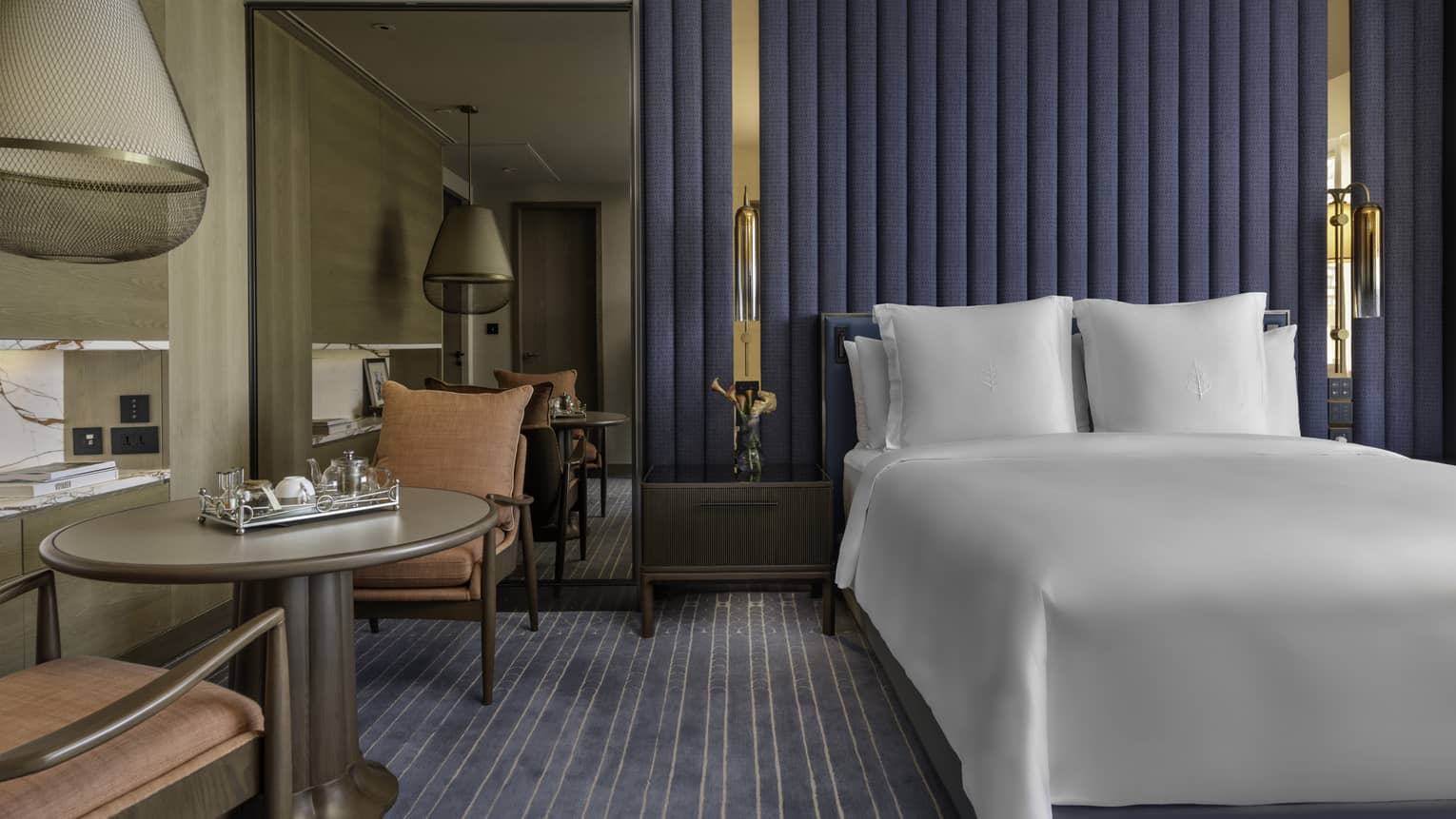 Renovated Superior Room with queen bed and white linens, blue striped carpet and accent wall, floor-to-ceiling mirror, table for two with salmon armchairs