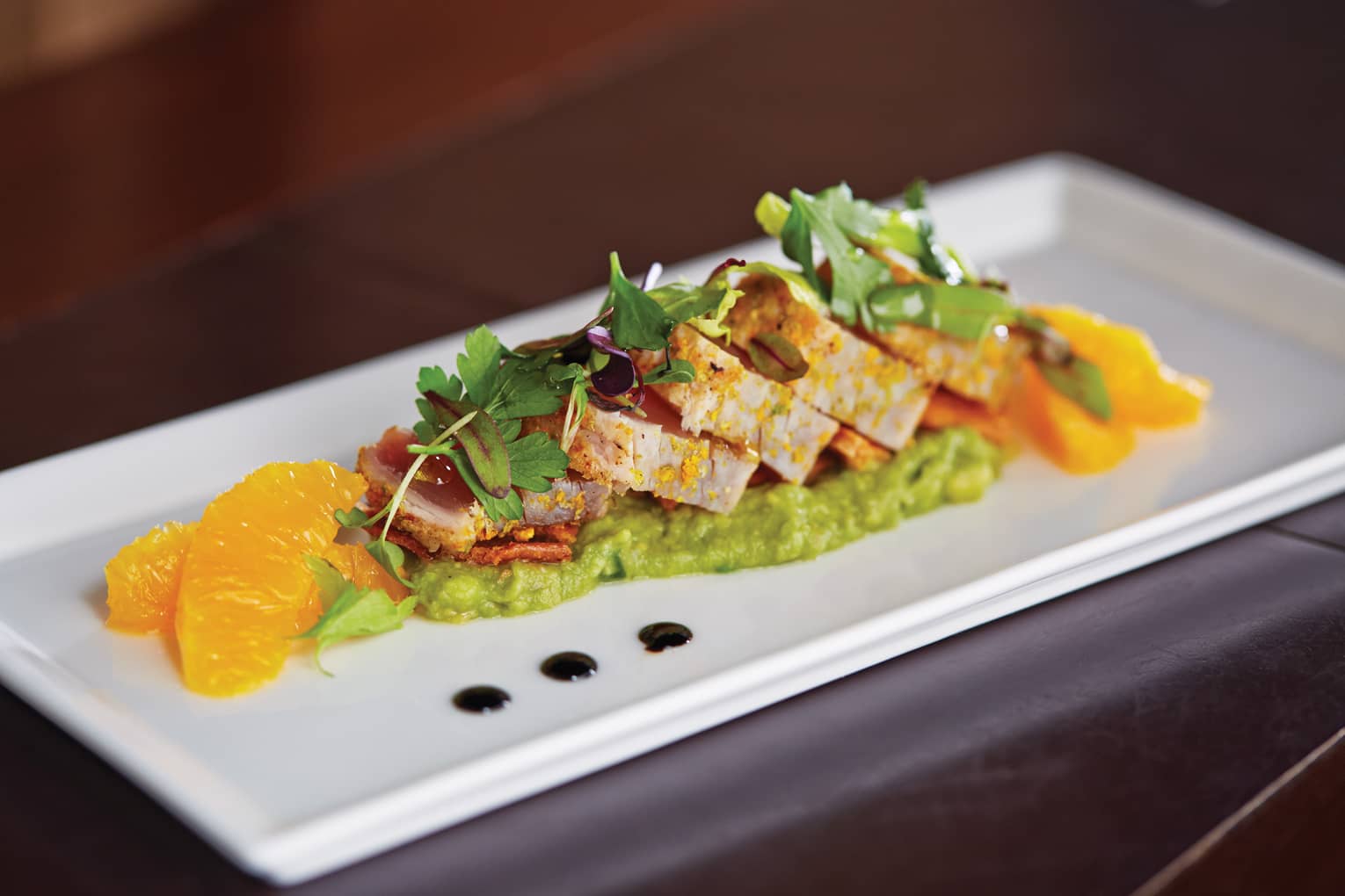 Sliced meat with green puree, spring lettuce, orange slices