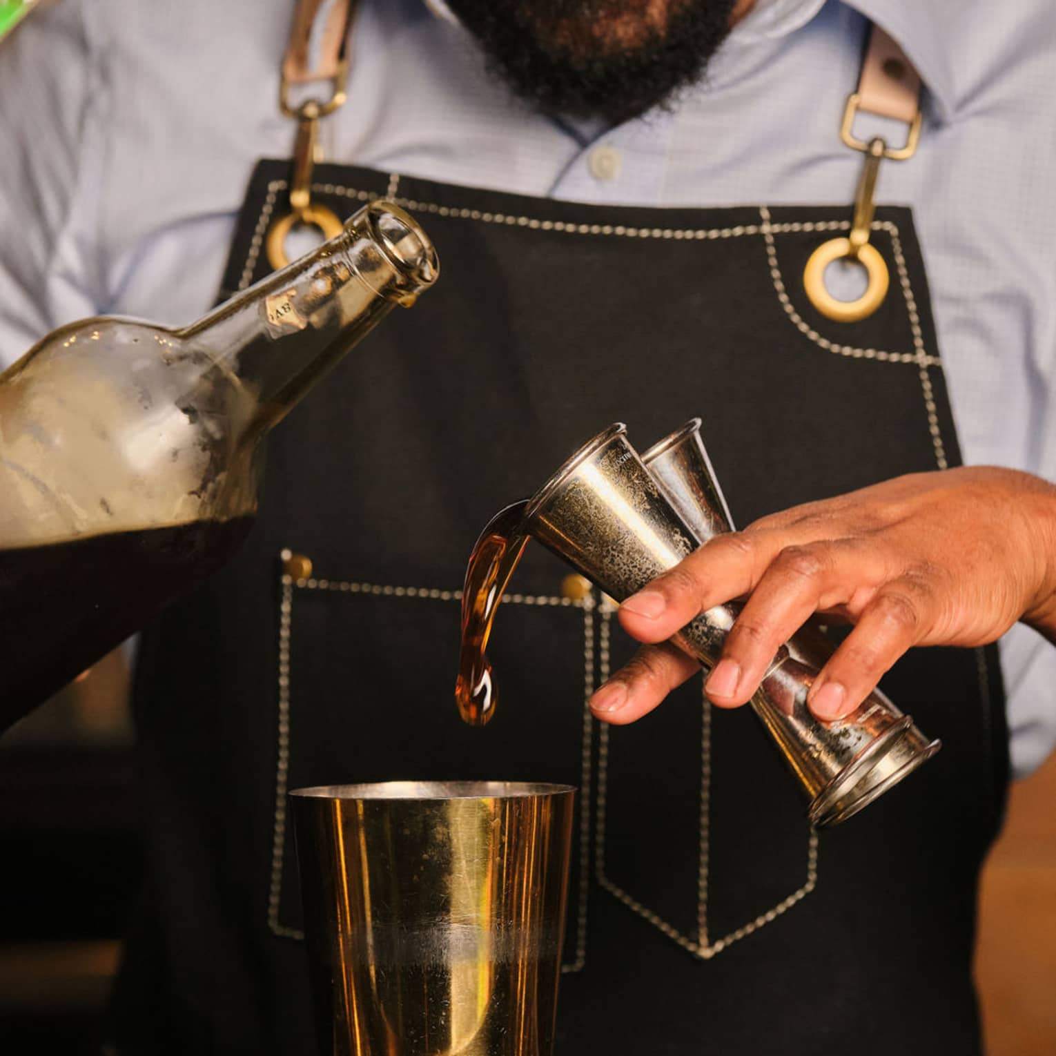 A bartender pours liquid from two jiggers into a cocktail shaker