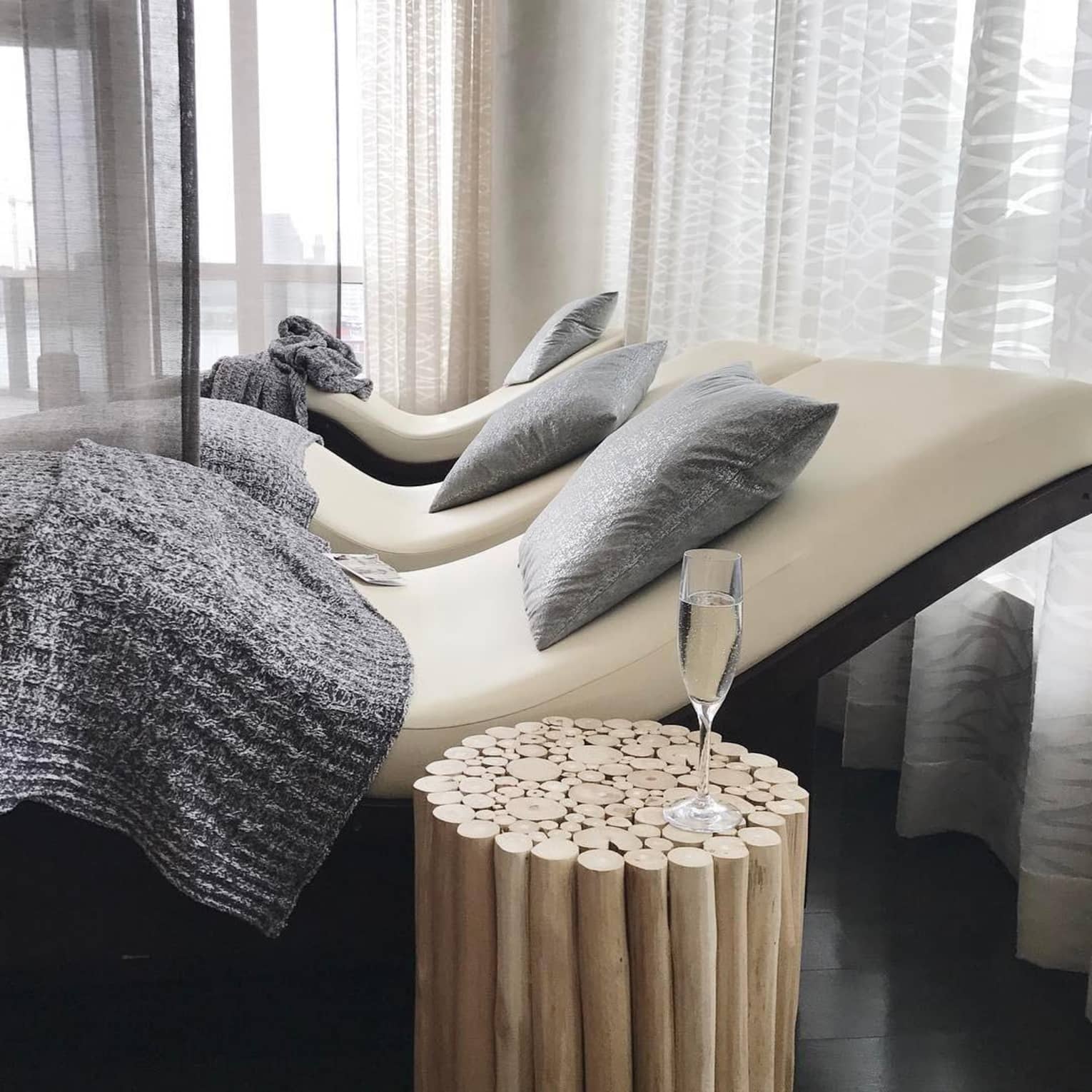 Champagne glass on table beside three curved spa beds with grey wool blankets, pillows