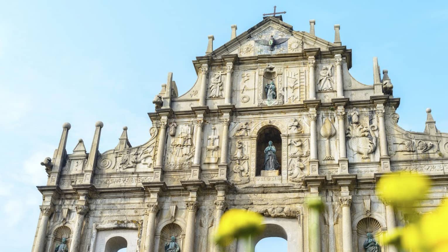 An ornate facade with archways at bottom, lined with thin towers and columns, intricate carvings and shelves holding statues.