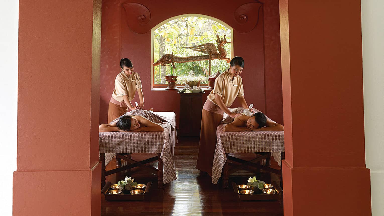 Couple lying on tables under sheets as spa staff rub their backs during Royal Heart Ritual massage