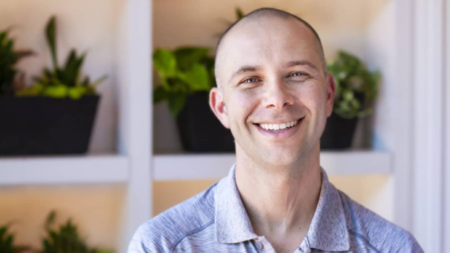 A man smiling with plants on shelves behind him.