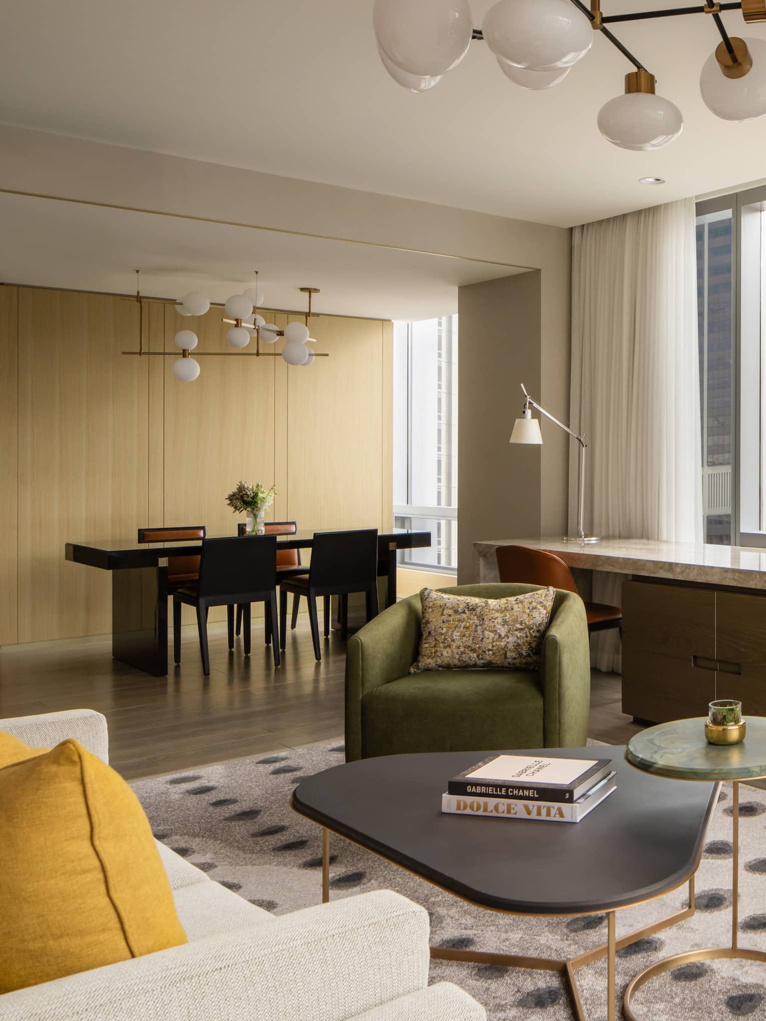 Luxury suite living area with a dining table and four chairs, desk, green armchairs, beige sofa, bar cabinet with glassware, TV and large windows