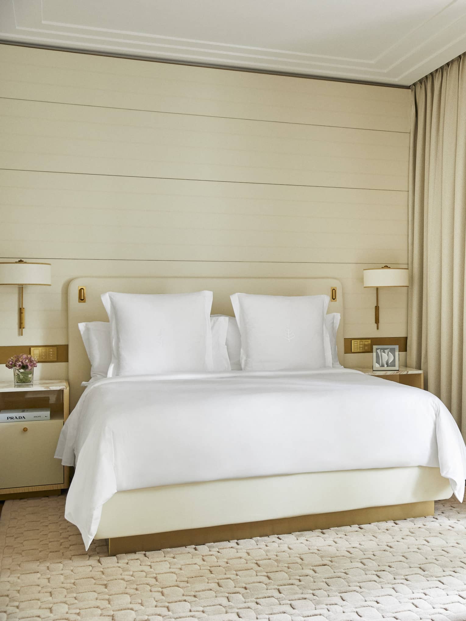 Light-filled hotel guest room with king bed, small round table with two chairs and creme-coloured curtains