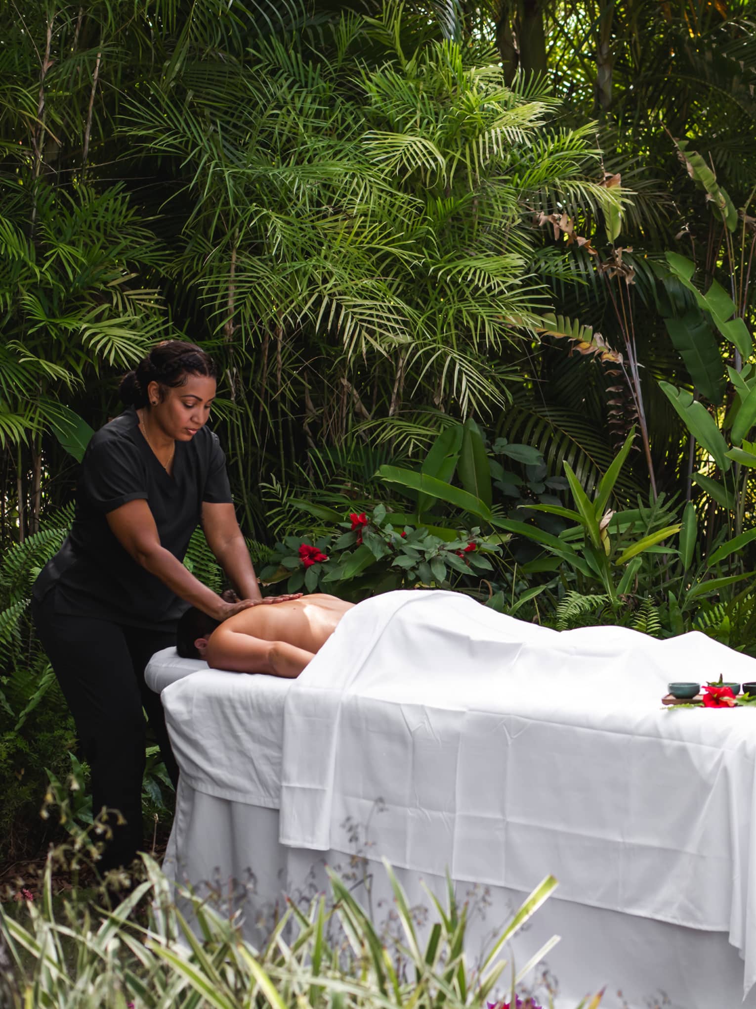 Guest receiving a massage by a massage therapist on a table set up among the foliage.