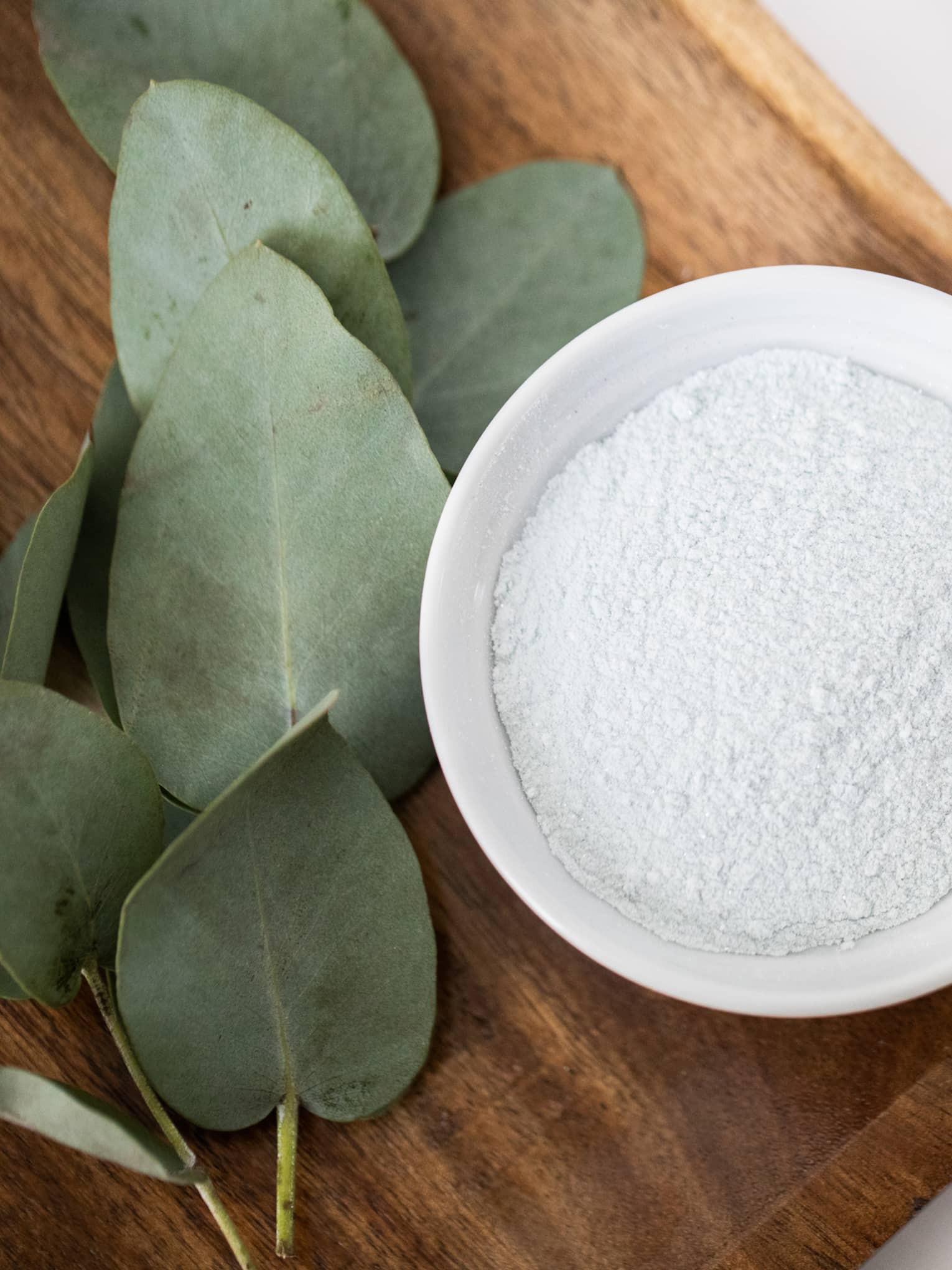 Spa ingredient in a white bowl placed on a wooden tray with eucalyptus leaves on the side