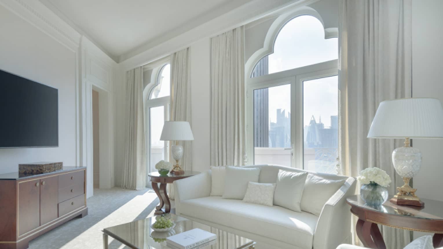A light-filled living room with white sofa, white arm chair, tan carpet, glass coffee table, lamps