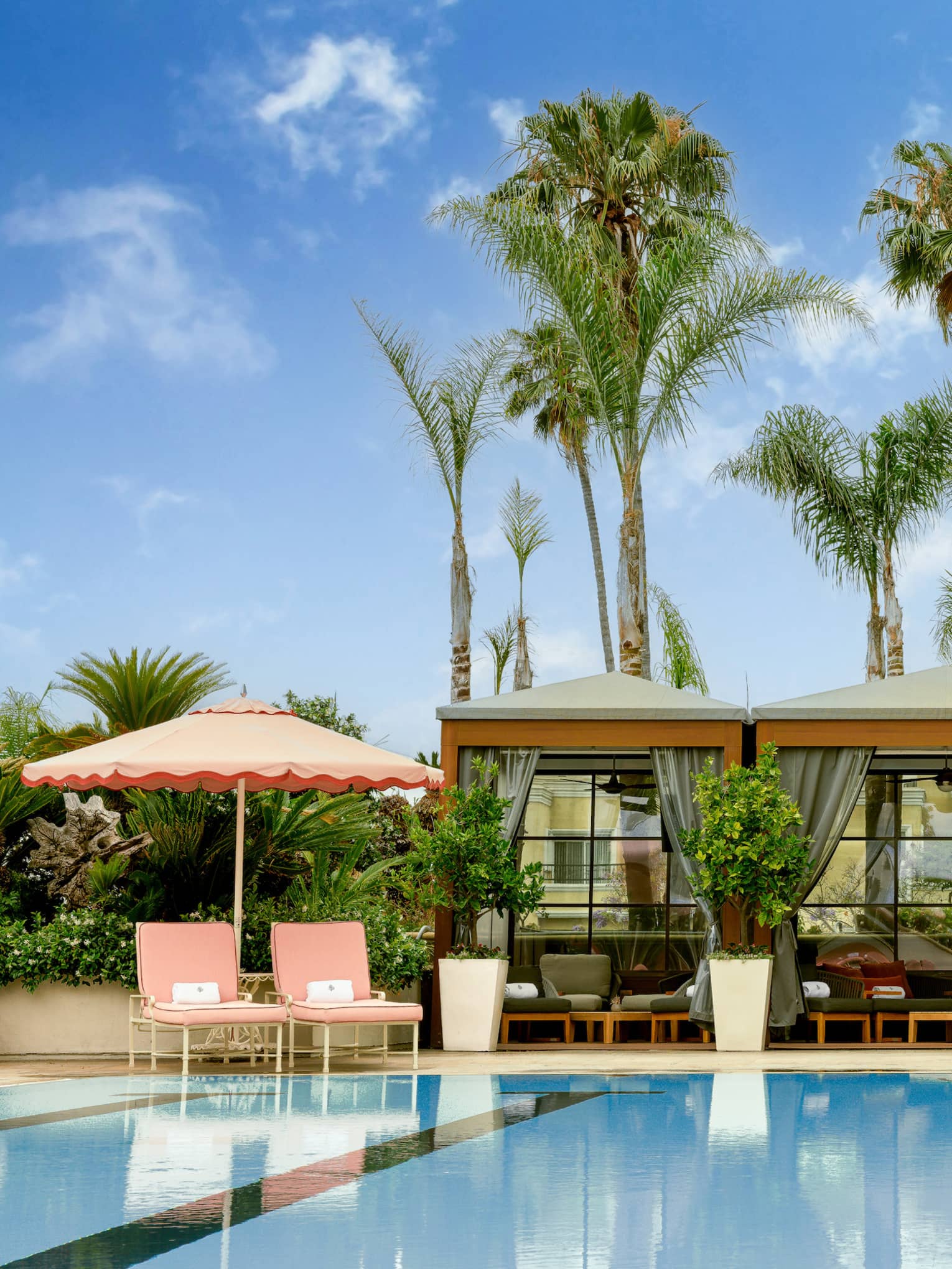 Outdoor pool surrounded by pink umbrellas and lounge chairs with palm trees in the background