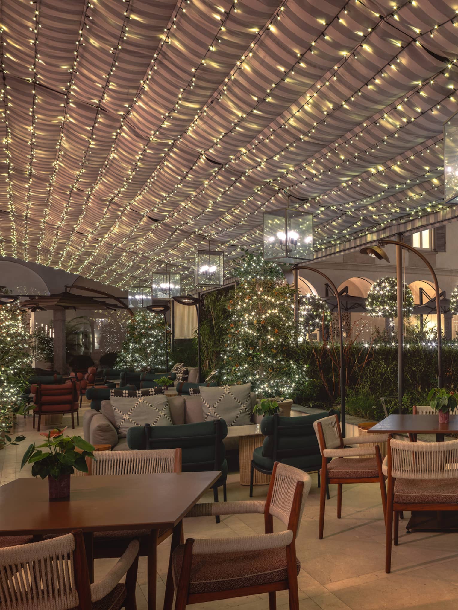 An outdoor dining area with holiday decor, including strings of holiday lights overhead