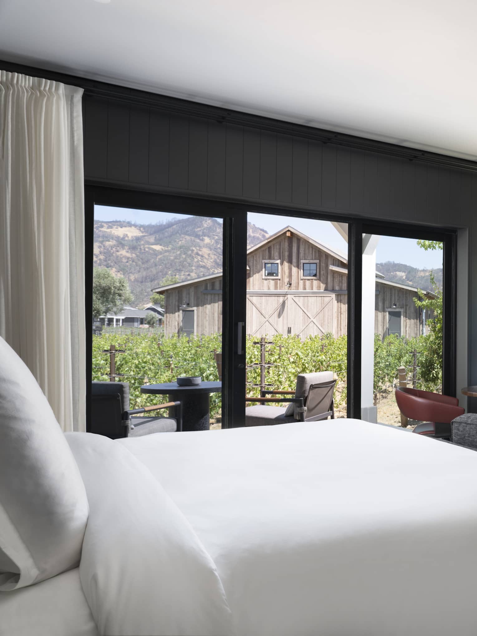 Luxury resort room with a king bed, cozy fireplace, vineyard view, seating area and outdoor patio facing rustic barn and mountains