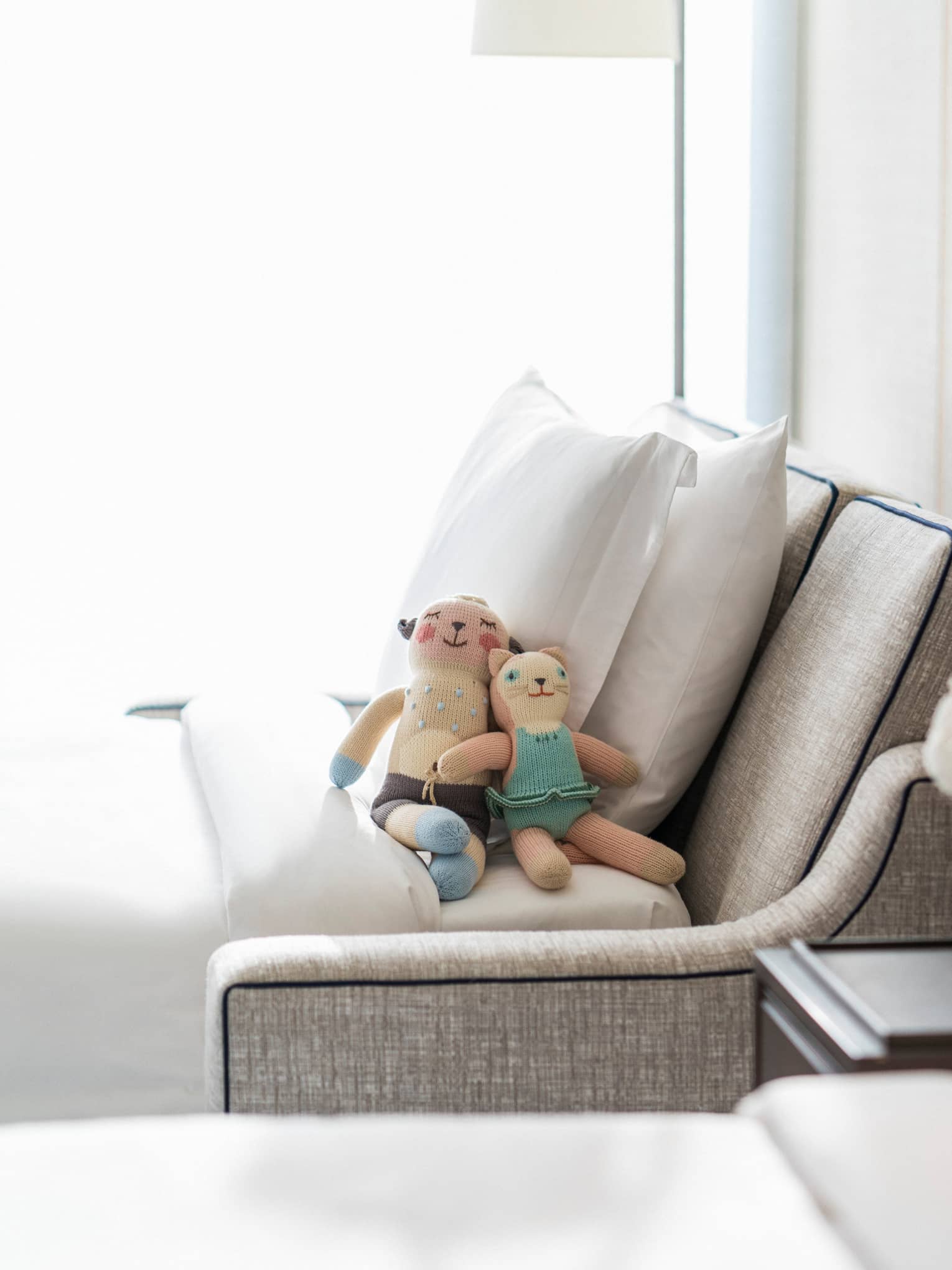 Two small stuffed toys rest against pillows on pull-out sofa beside hotel bed