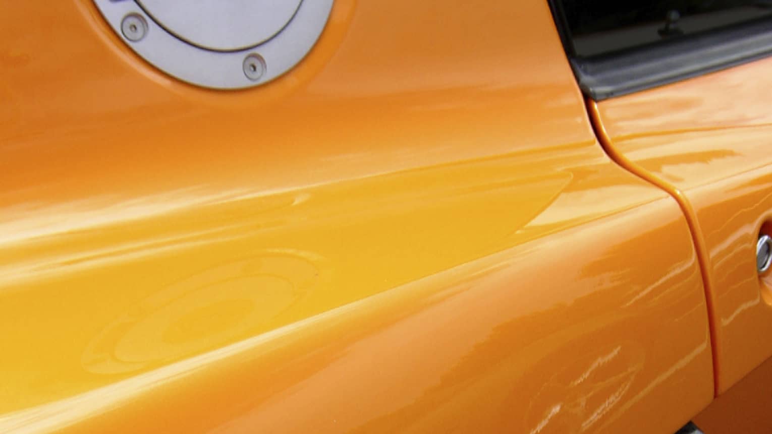 Extreme close-up of the side of a glossy, tangerine orange sportscar with silver and carbon grey accents.
