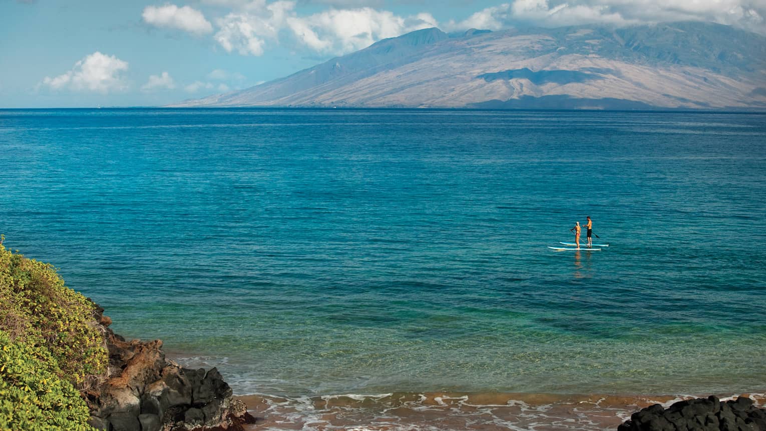 View from shore looking out at man and woman on stand-up paddleboards on ocean
