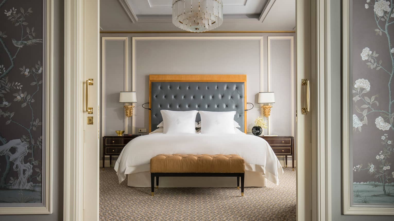 Executive Deluxe Suite front view of king-size bed with tall padded blue headboard, gold velvet bench at foot