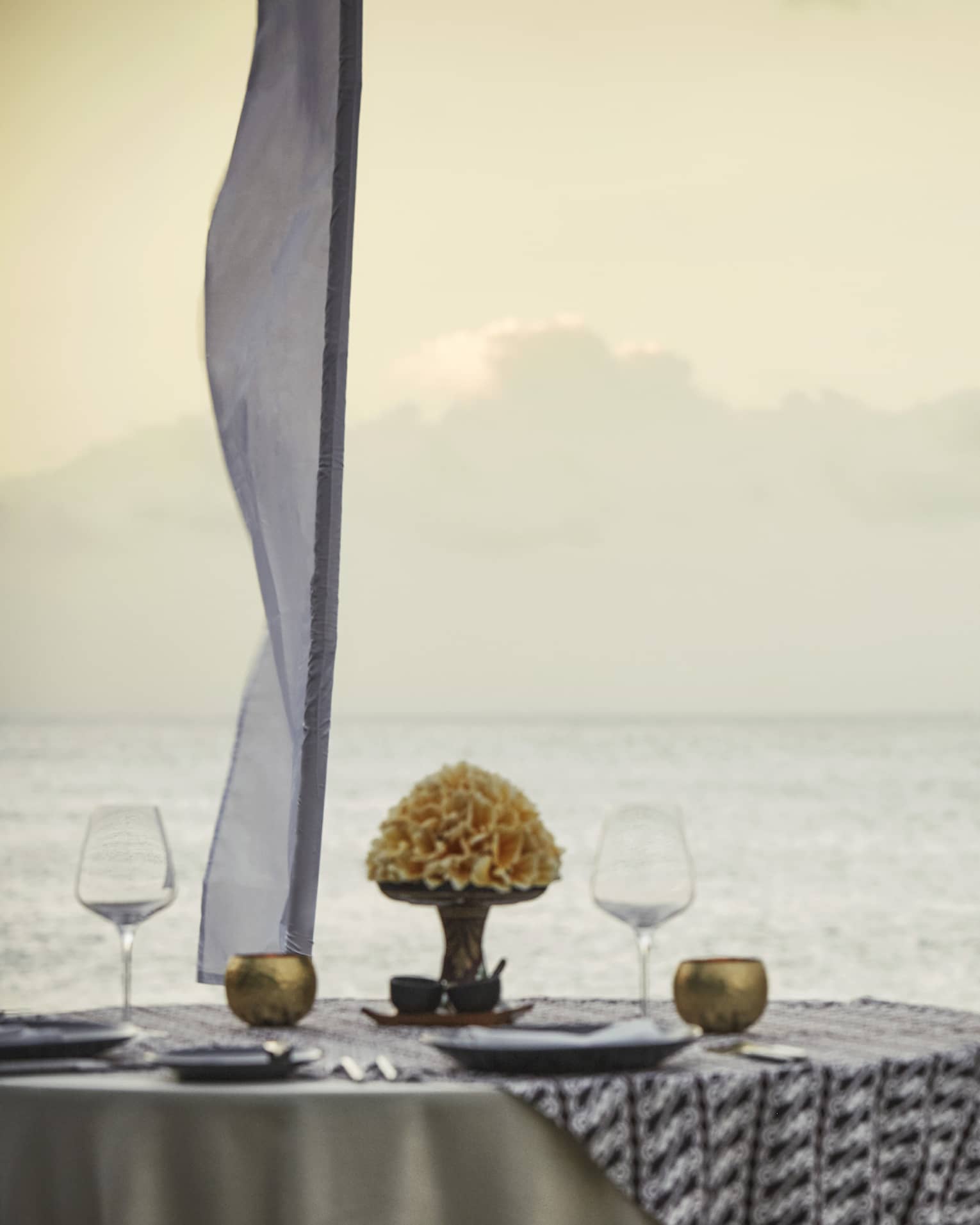 Couple embraces beside private dining table overlooking ocean at sunset