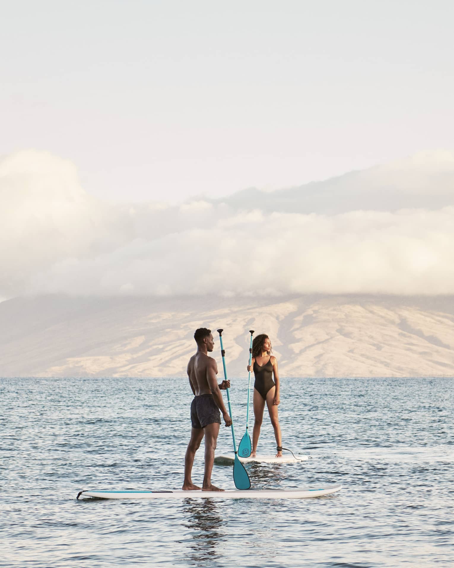 Man and woman stand on SUP paddleboards in the ocean in Maui