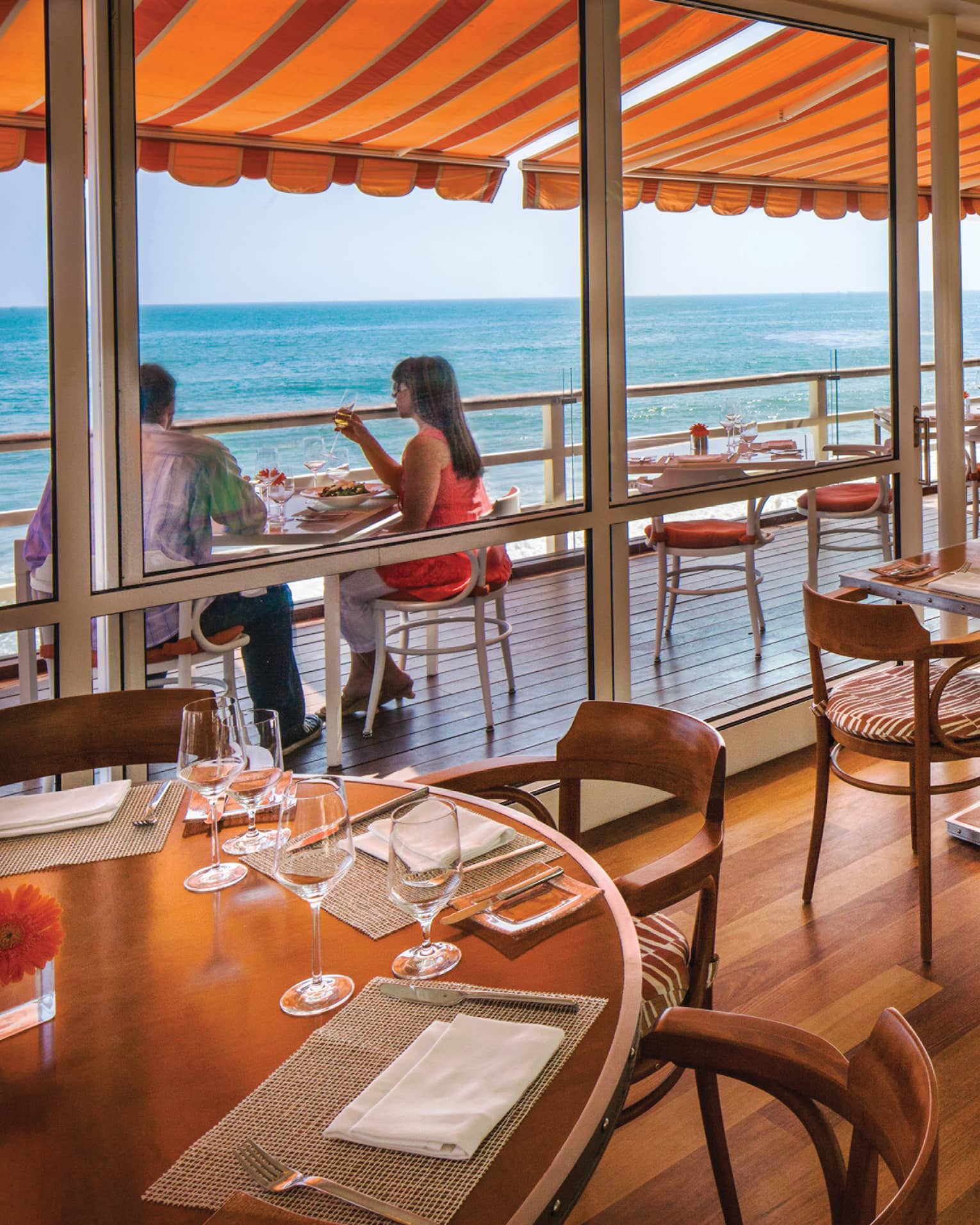 Dining tables chairs on hardwood floors, sliding glass wall to diners under orange awning