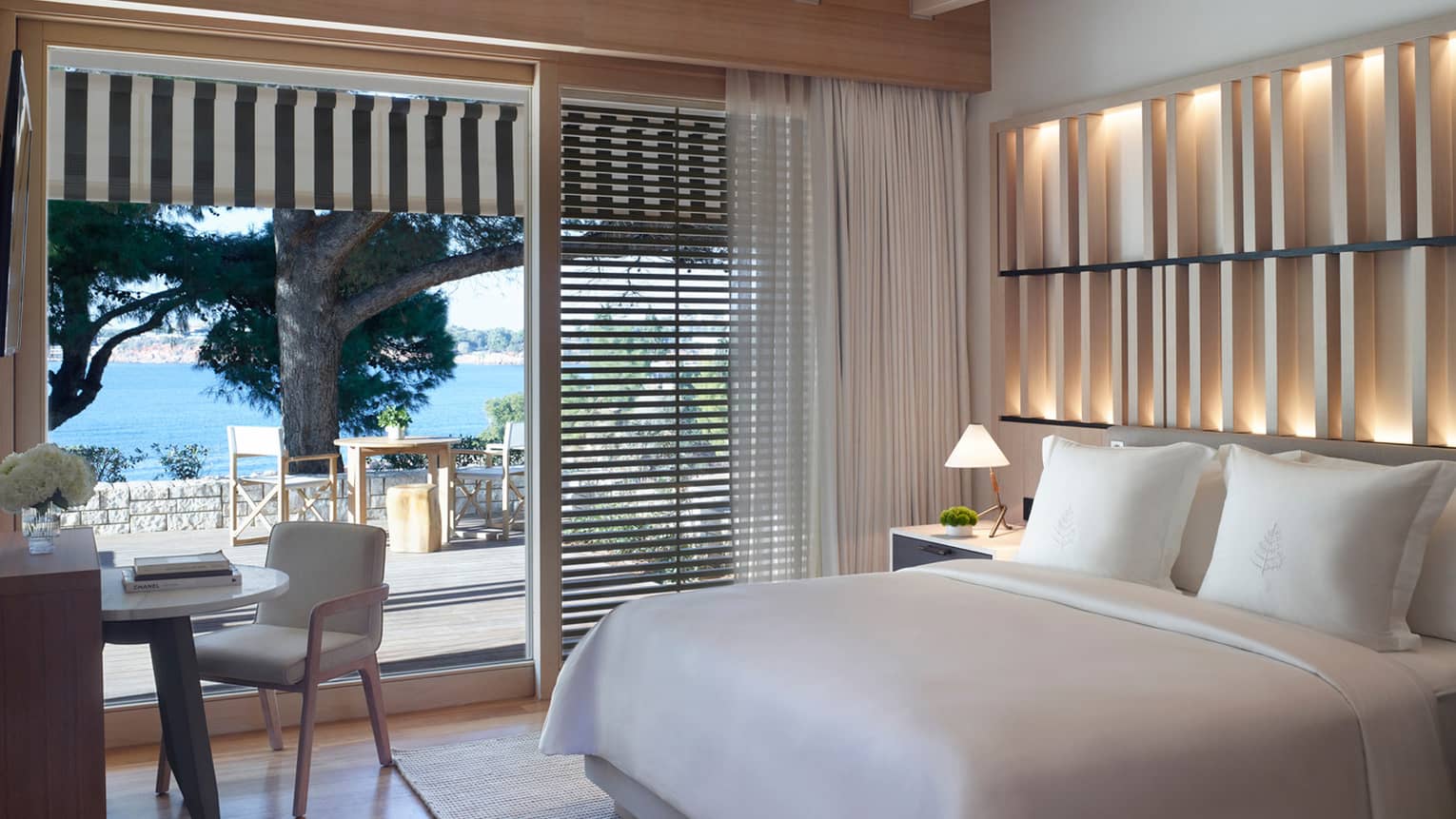 Bedroom with an illuminated wooden accent wall, white king bed, desk and chair, and sliding door to patio