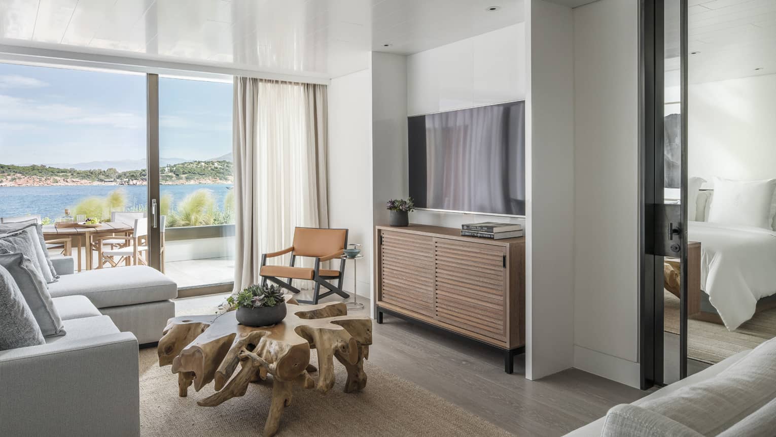 Nafsika Sea View Suite with white sectional sofa, flat screen TV, carved wood coffee table, sliding glass doors opening onto balcony, ocean views