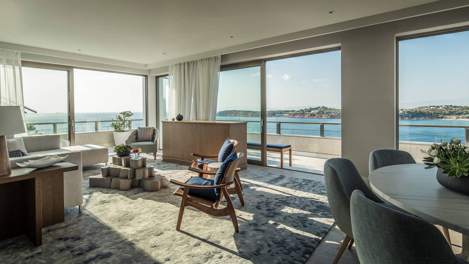 Arion Presidential Suite living area with white sectional sofa, navy arm chairs, dining table, panoramic views of Mediterranean Sea