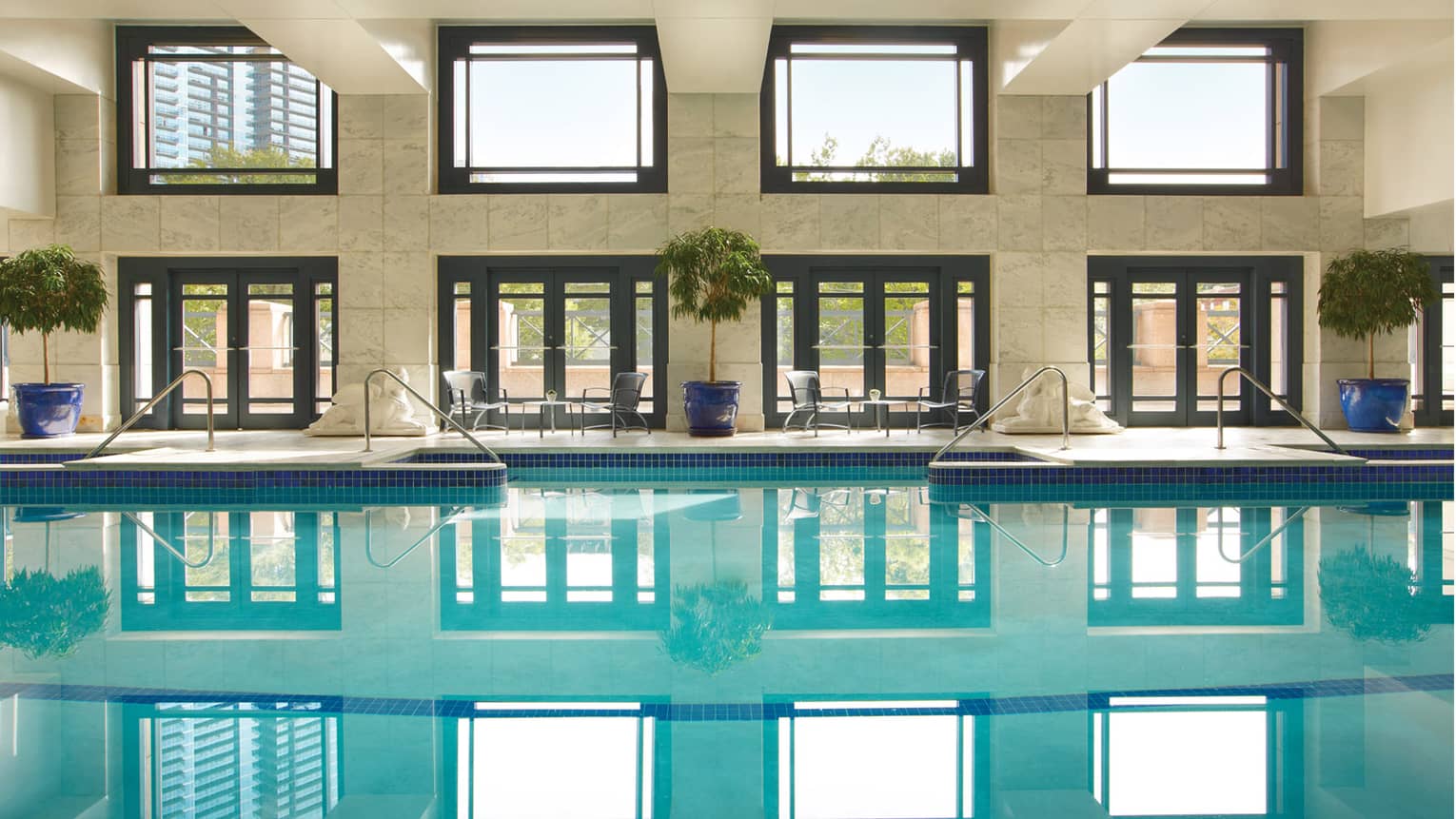 Indoor swimming pool under marble wall, light from large windows reflected on water