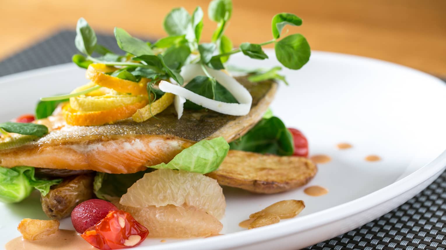 Baked fish filet on roasted vegetables, garnished with fresh fruit, sprouts